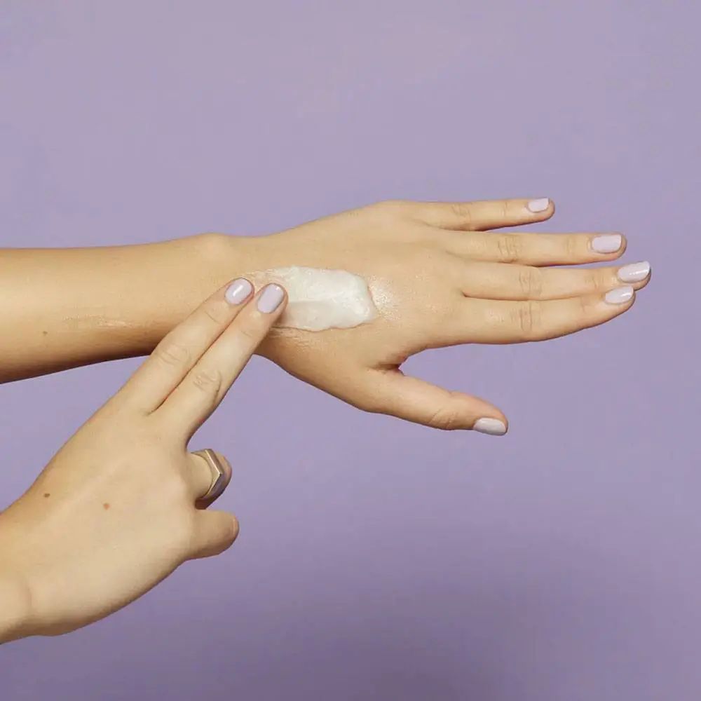 Mains avec produit sur la paume. Sur fond violet.