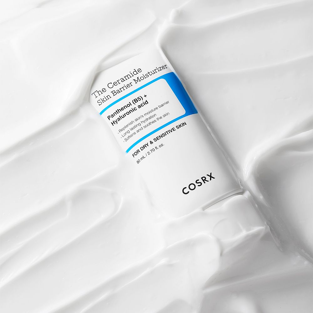 Crème hydratante COSRX The Ceramide Skin Barrier dans un tube blanc, entourée de crème blanche.