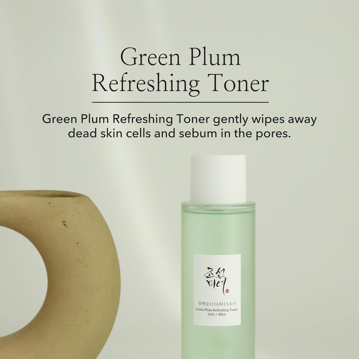 Productfles naast een decoratief object. Tekst: Green Plum Refreshing Toner. Productbeschrijving.