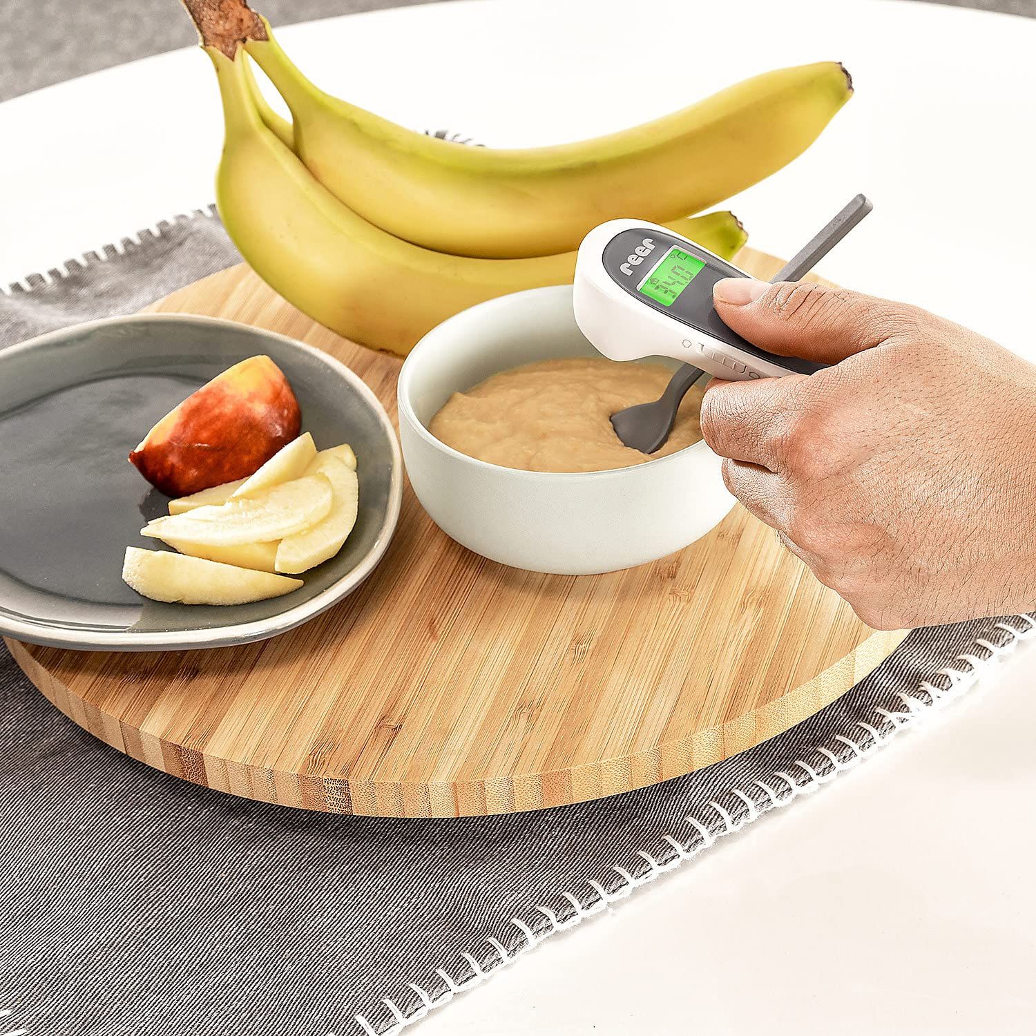 Hand houdt thermometer bij voorhoofd lachende baby, display toont 36.5°C.