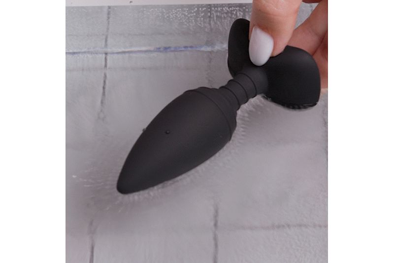 Zwarte anale plug, vastgehouden door een hand. De plug heeft een conische vorm en een geribbeld middengedeelte.