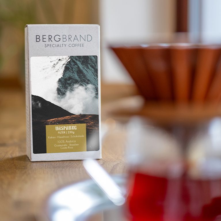 Paquet de café avec motif de montagne. Texte : BERGBRAND, Ursprung, Filter, 250g. Ingrédients : cacao, noisette, chocolat, 100% Arabica.