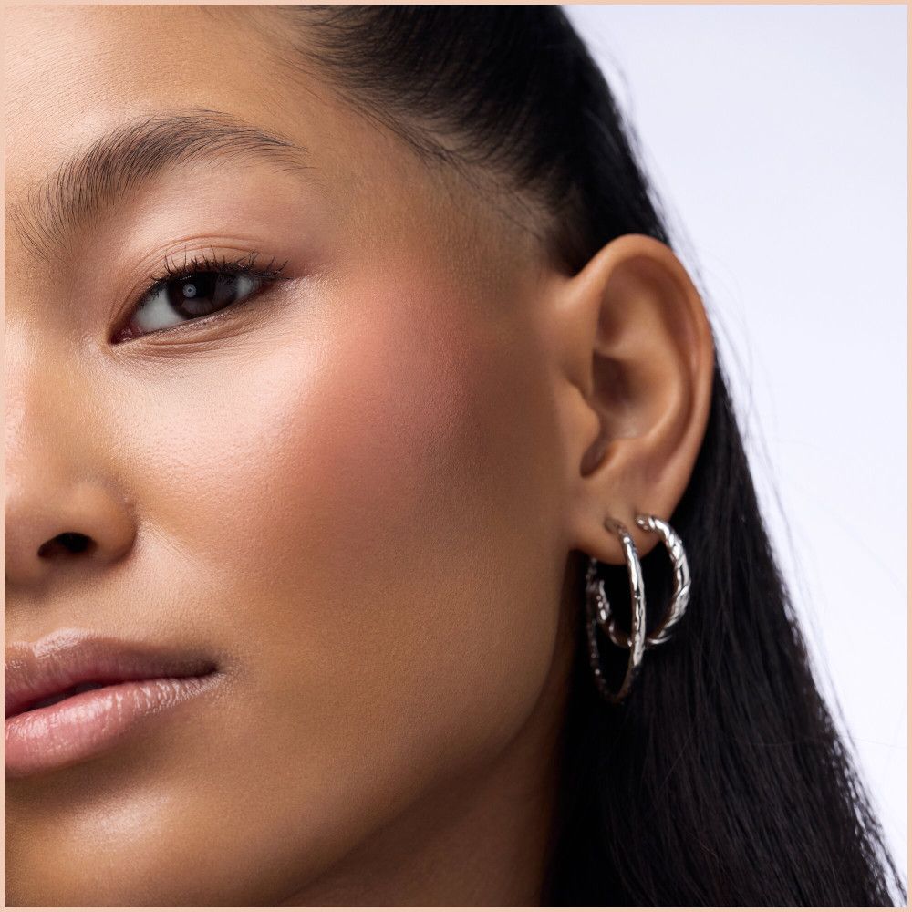 Gros plan sur un visage avec du blush rose sur la joue. La femme porte des créoles argentées.