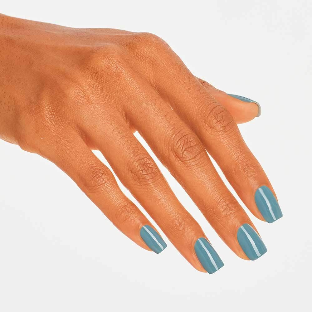 Hand met blauw-grijze gelakte nagels. De nagels zijn vierkant van vorm. Een witte streep loopt langs het midden.