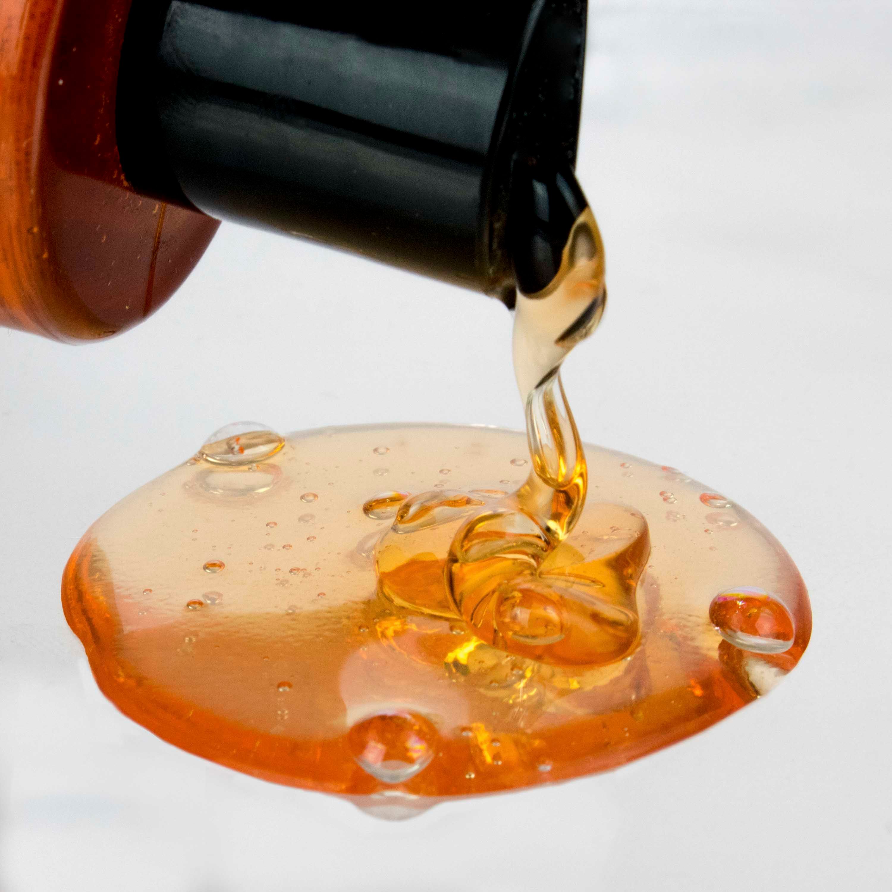 Uitlopende shampoo met arganolie. Bruine vloeistof. Op lichte ondergrond. Productnaam niet zichtbaar.