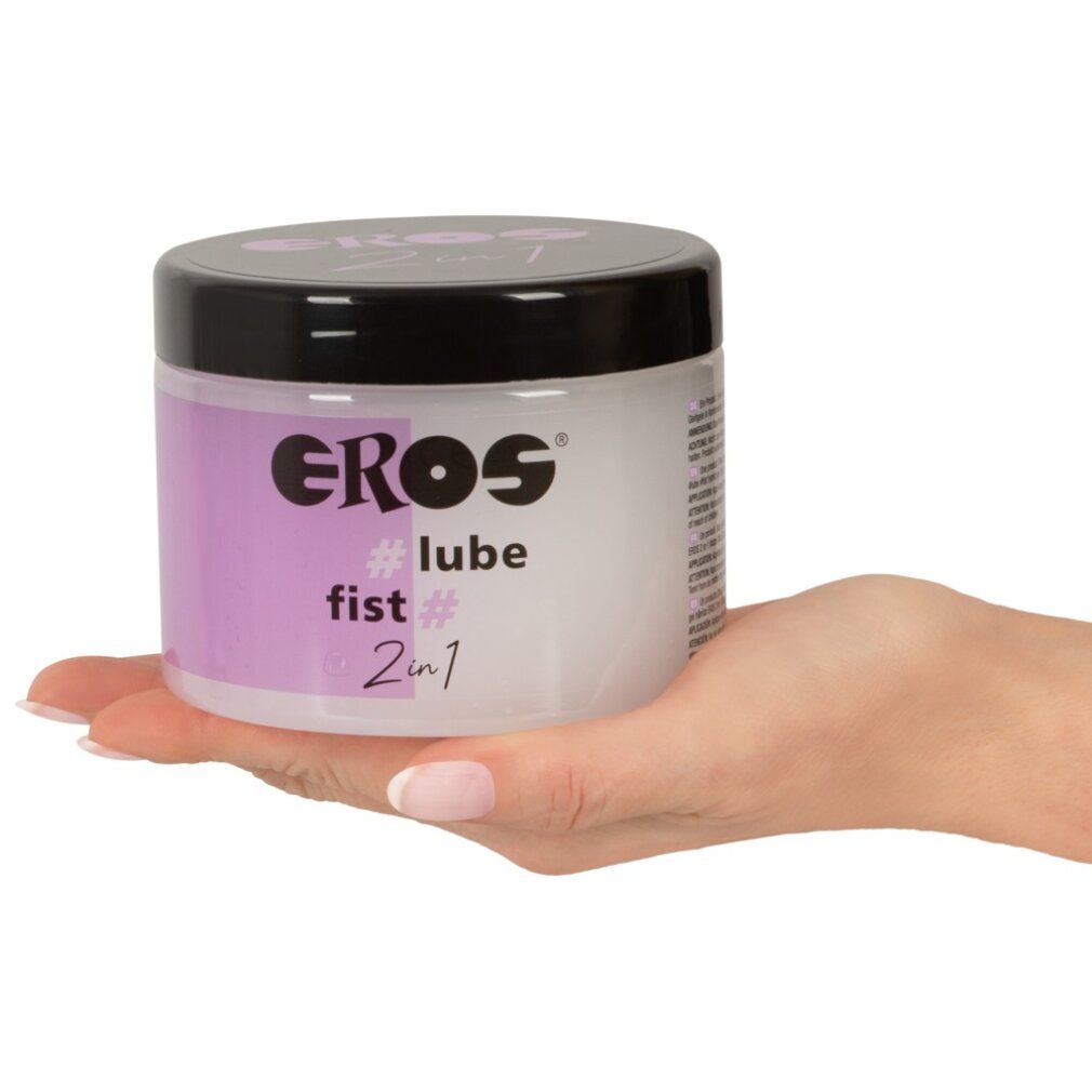 Main tenant un récipient. L'étiquette indique EROS, #lube, fist # et 2in1. Fond violet.