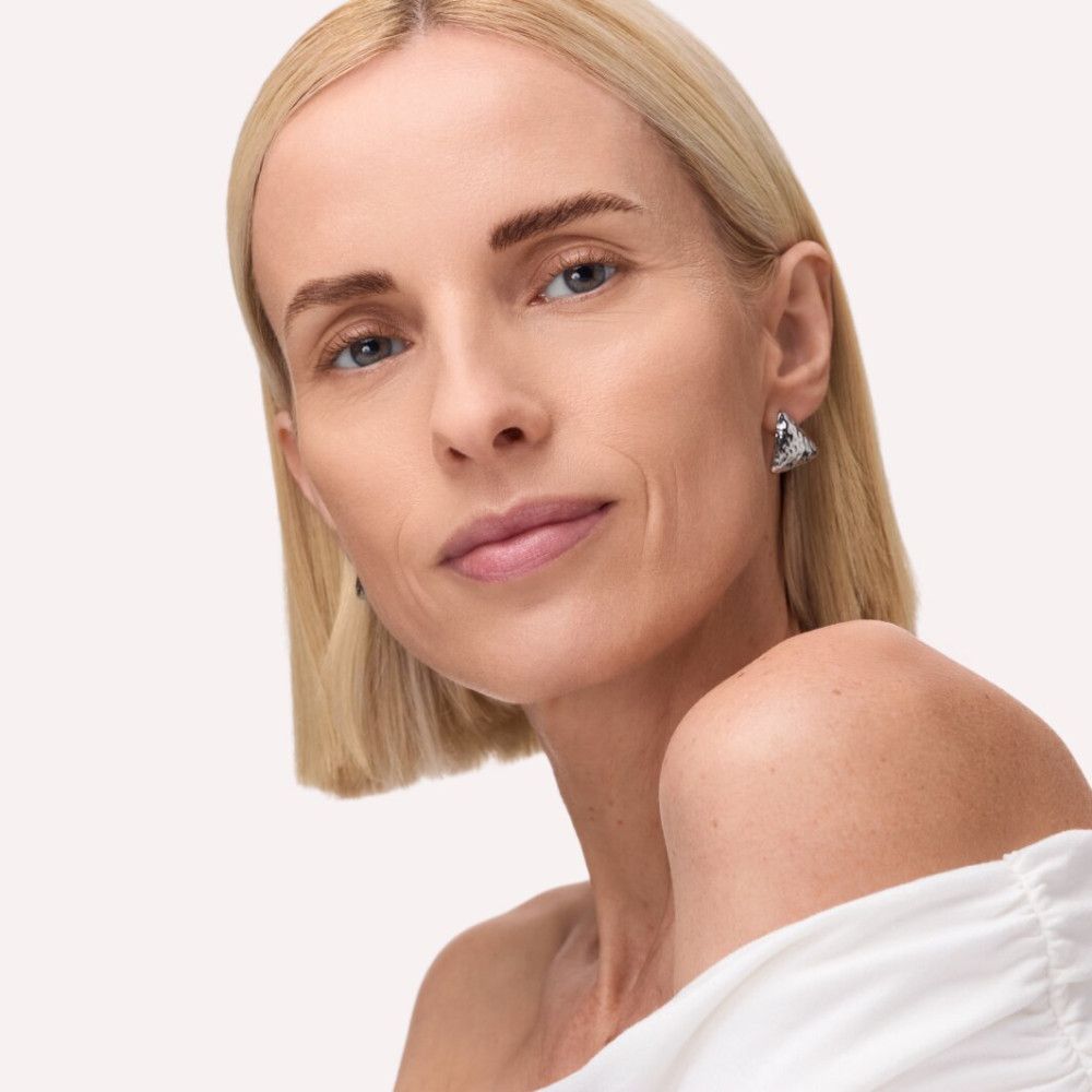 Portret van een vrouw met blond haar en blauwe ogen. Ze draagt oorbellen.