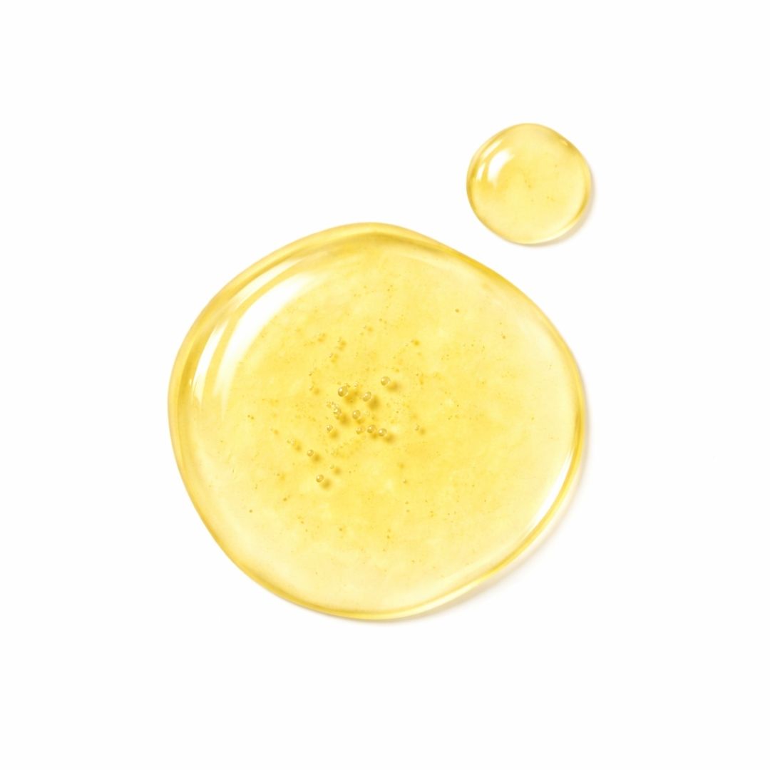 Deux gouttes de liquide jaune sur fond blanc. La plus grande goutte a des bulles.