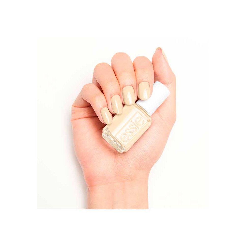 Hand met gelakte nagels en nagellakflesje. Flesje met witte dop, opschrift "essie". Nagellak in licht beige.