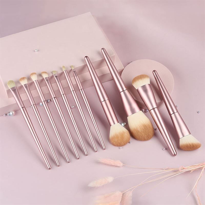 Make-up kwastenset. Roze handvatten, lichte borstelharen. Verschillende vormen en maten. Op roze achtergrond.