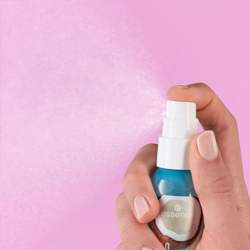 Hand houdt een sprayfles vast. De sproeikop wordt bediend, nevel is zichtbaar. Achtergrond: roze.