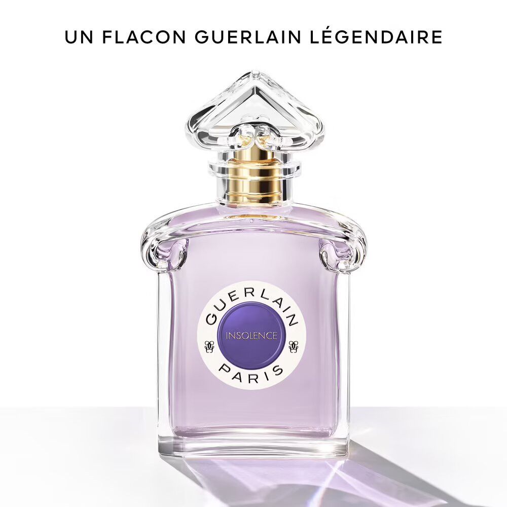 Flacon en verre avec liquide violet. Étiquette "INSOLENCE PARIS". Bouchon doré. Vaporisateur transparent. Texte : "UN FLACON GUERLAIN LÉGENDAIRE".