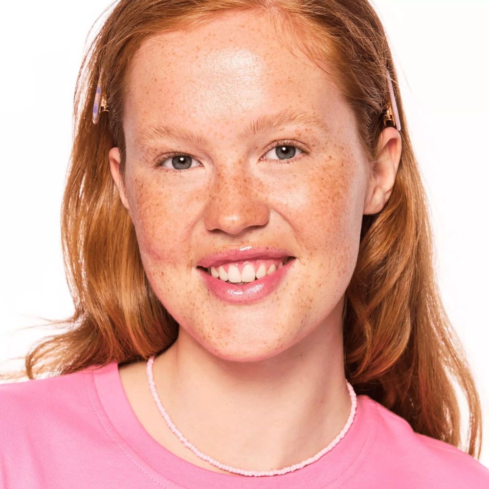 Portrait d'une femme avec des taches de rousseur. Elle porte un haut rose et un collier. Cheveux avec pinces.