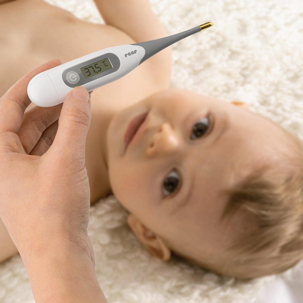 Un thermomètre est utilisé sur un bébé. Le thermomètre affiche 37,5°C. Marque : reer.