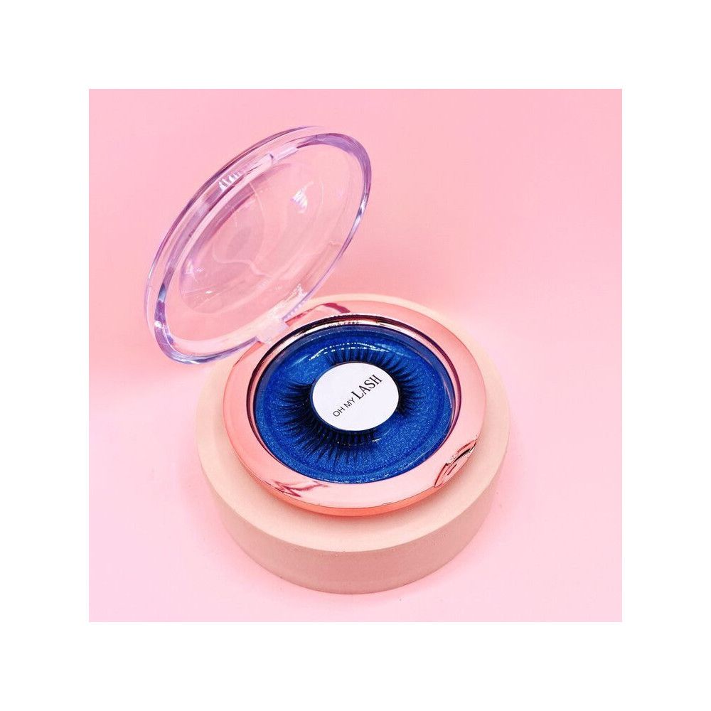 Boîte ronde dorée rose avec couvercle transparent ouvert. Intérieur bleu avec faux cils. Étiquette blanche avec "OH MY LASH".