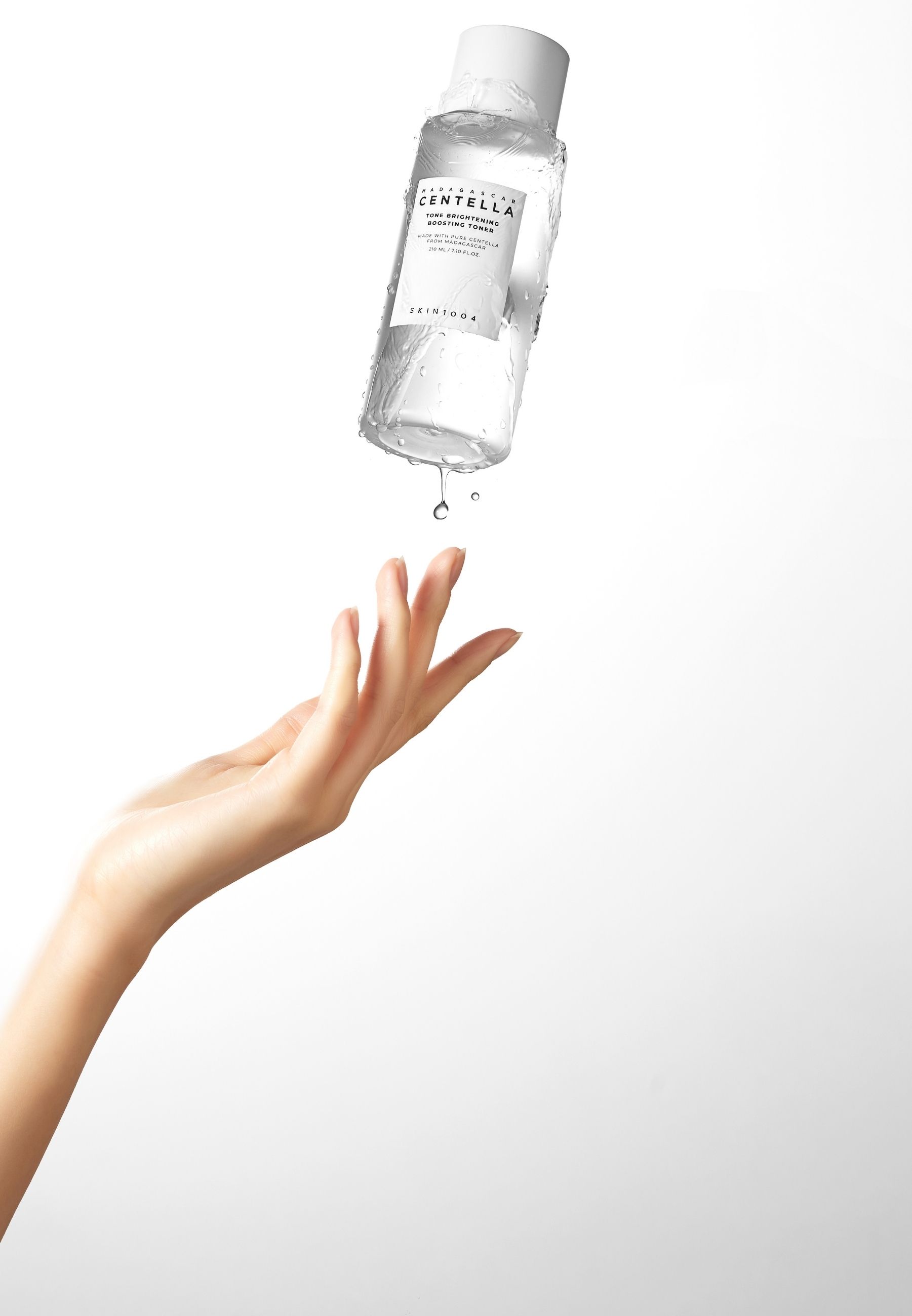 Une main attrape une goutte de liquide qui coule d'une bouteille. Bouteille avec étiquette du produit.