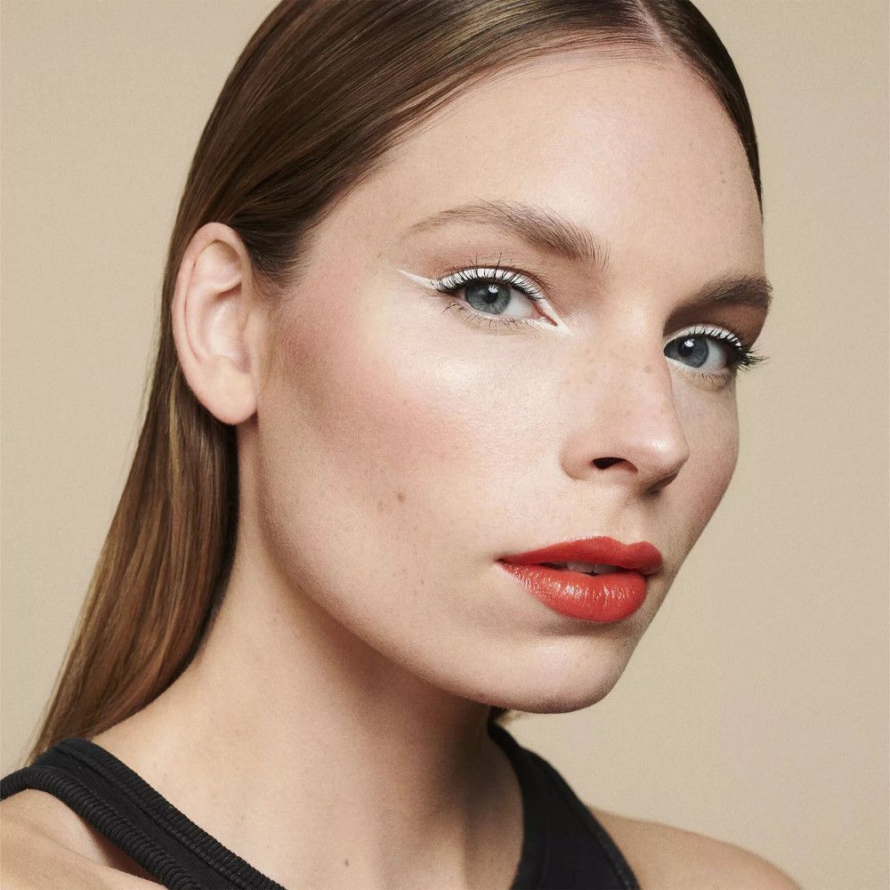 Femme avec trait de khôl blanc sur la paupière supérieure et rouge à lèvres rouge.