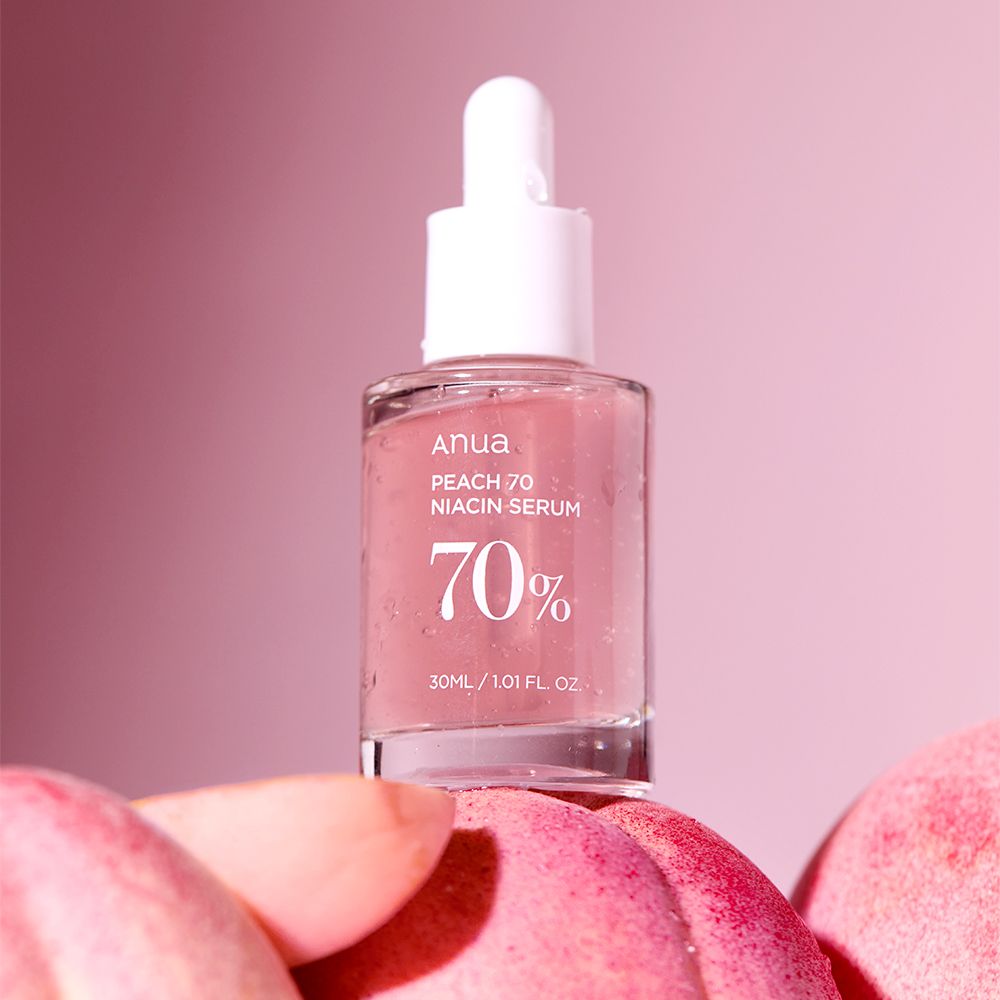 Anua Peach 70 Niacin serumfles op perziken, roze achtergrond.