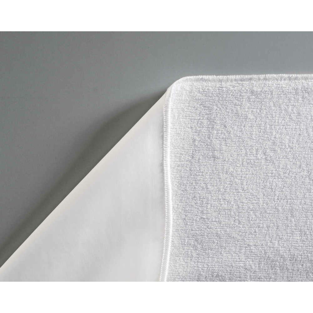 Gros plan d'un sur-matelas en éponge blanc avec un fond blanc. Le bord est ourlé. Le tissu est texturé.