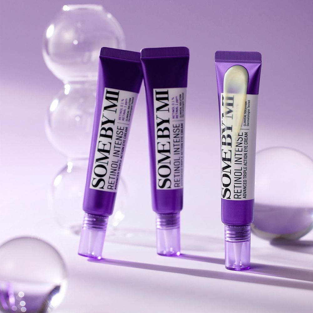 Trois tubes de crème contour des yeux SOMEBYMI Retinol Intense sur fond violet avec des sphères en verre.