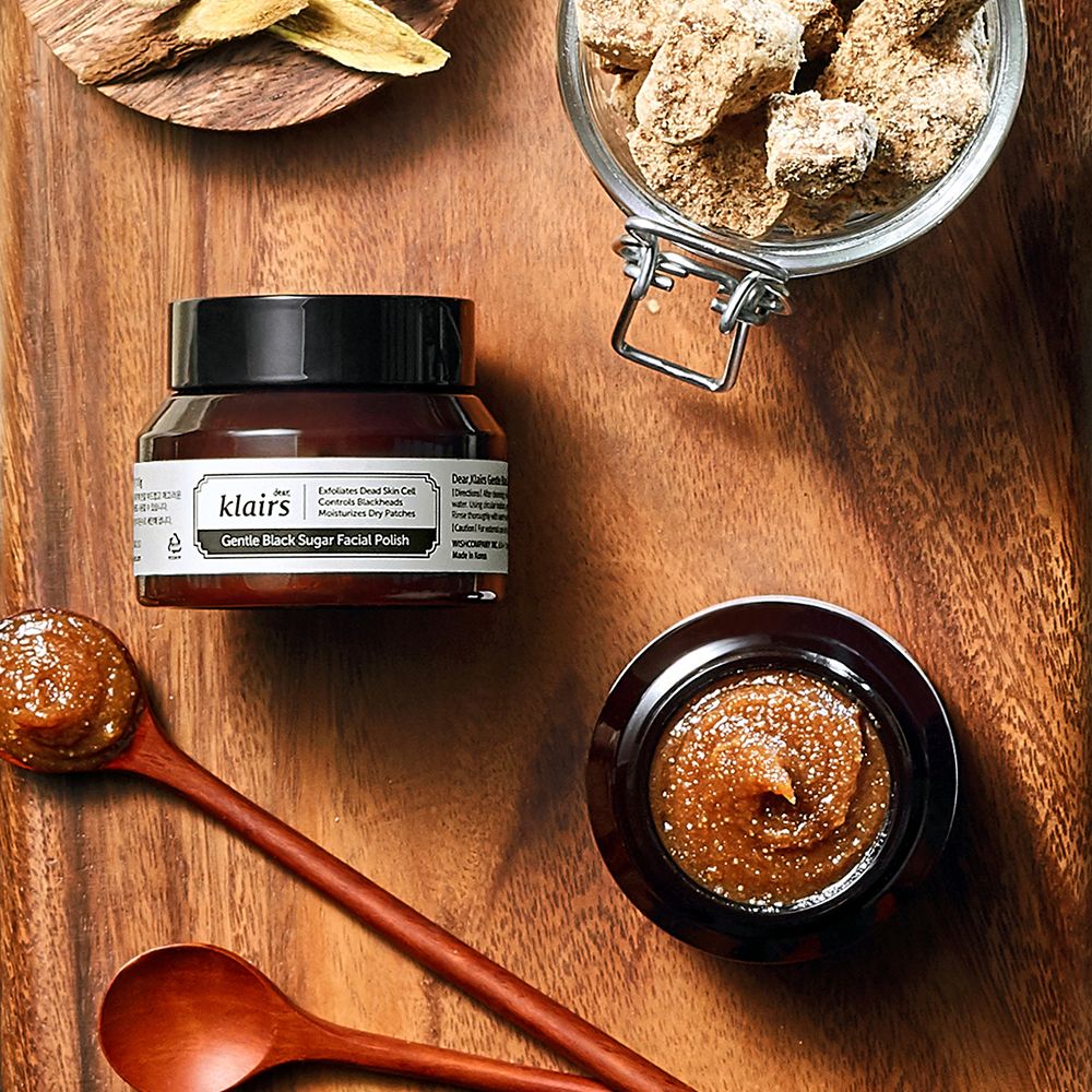 Klairs Gentle Black Sugar Facial Polish op een houten tafel met ingrediënten zoals bruine suiker.