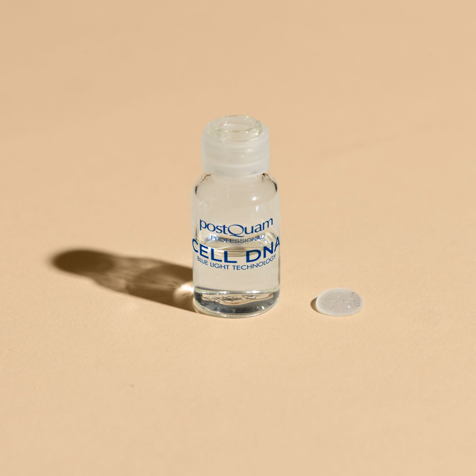 Petite bouteille avec liquide. Inscription: Postquam, CELL DNA, Blue Light Technology. Une goutte à côté.