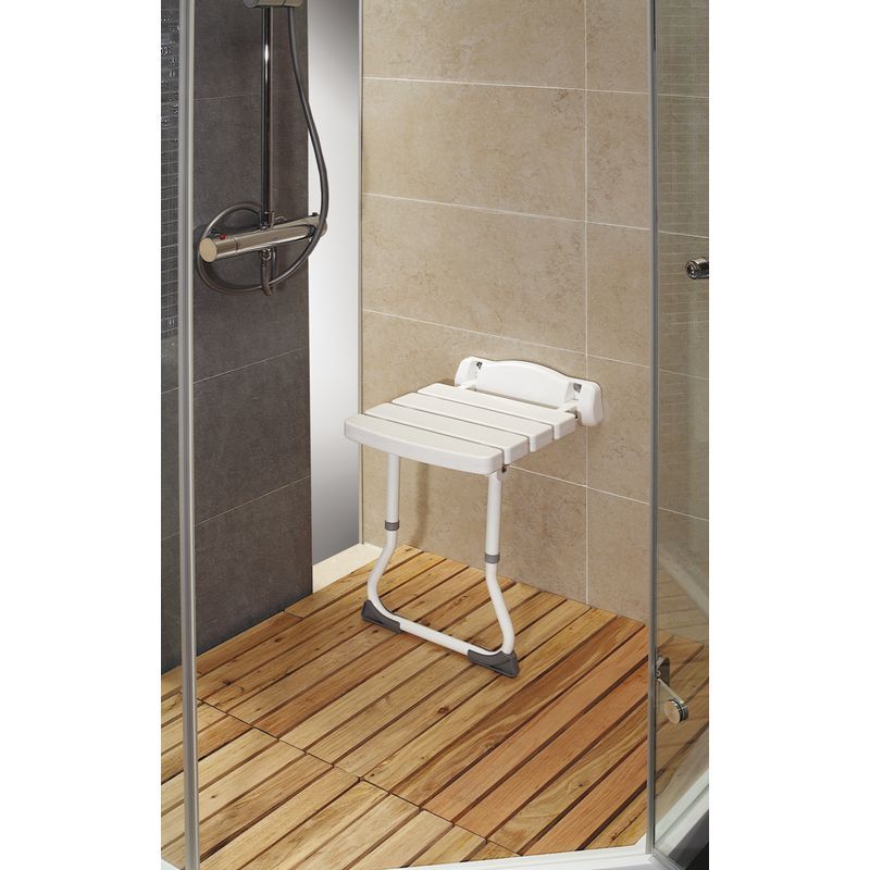Siège de douche pliable avec support au sol. Siège blanc à lattes, fixé au mur. Cadre en aluminium, dans une cabine de douche.