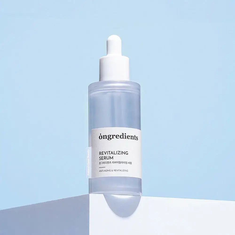 ONGREDIENTS Revitalizing Serum. Transparante fles met witte dop en pipet. Geplaatst op blauwe achtergrond.