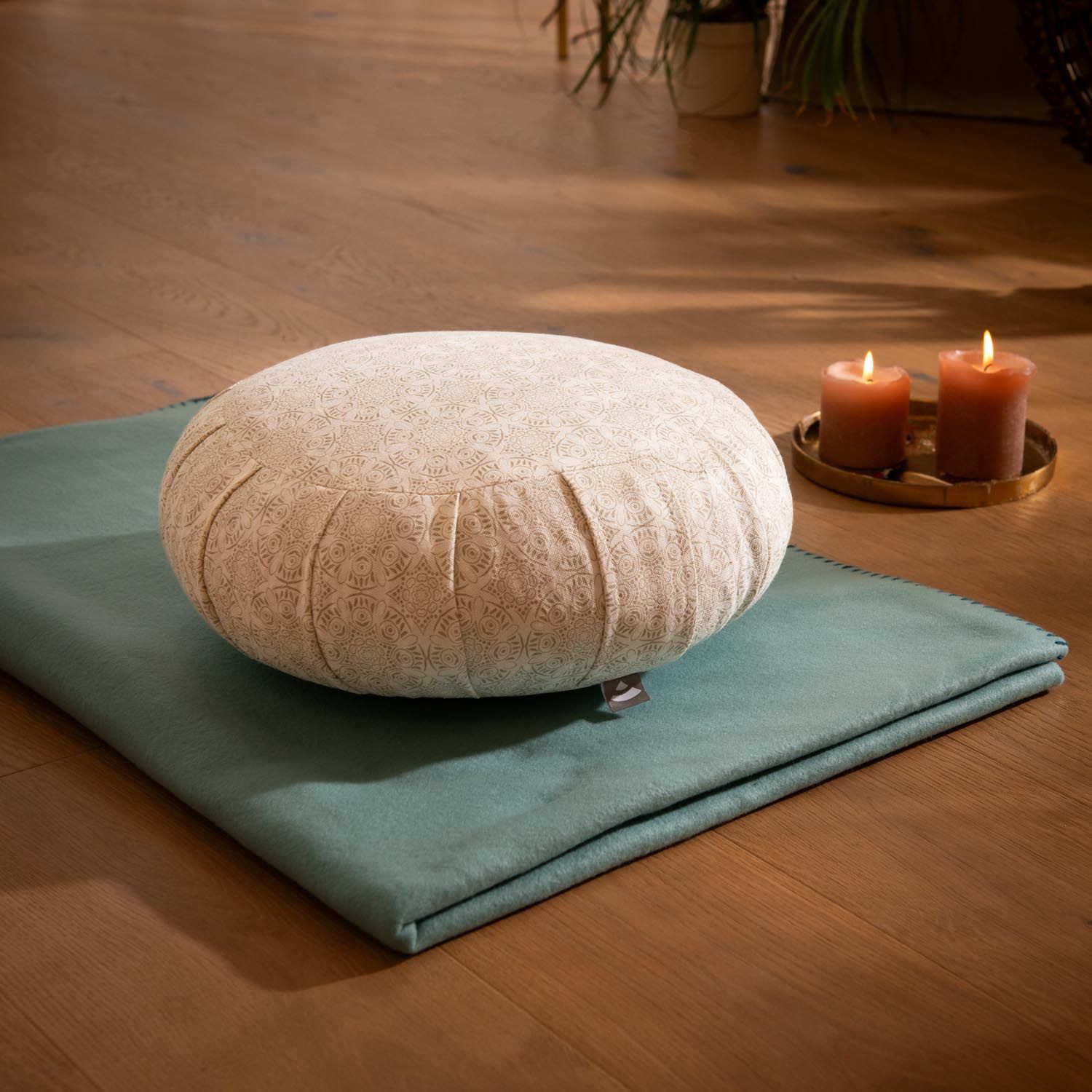 Coussin de méditation Bodhi Zafu avec motif sur tapis turquoise, bougies en arrière-plan.