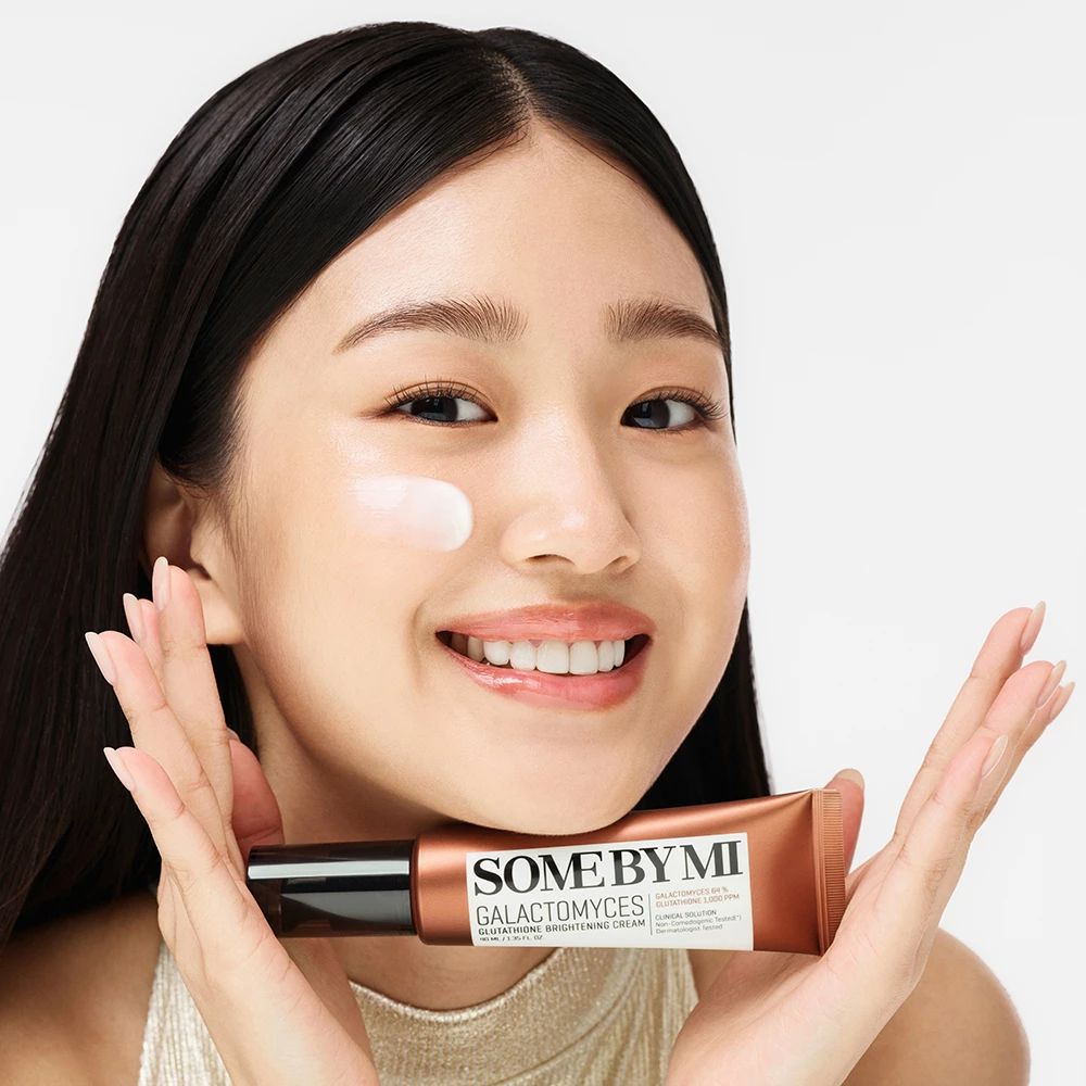 Femme tient un tube de crème SOME BY MI Galactomyces. Crème appliquée sur la peau. Elle sourit.