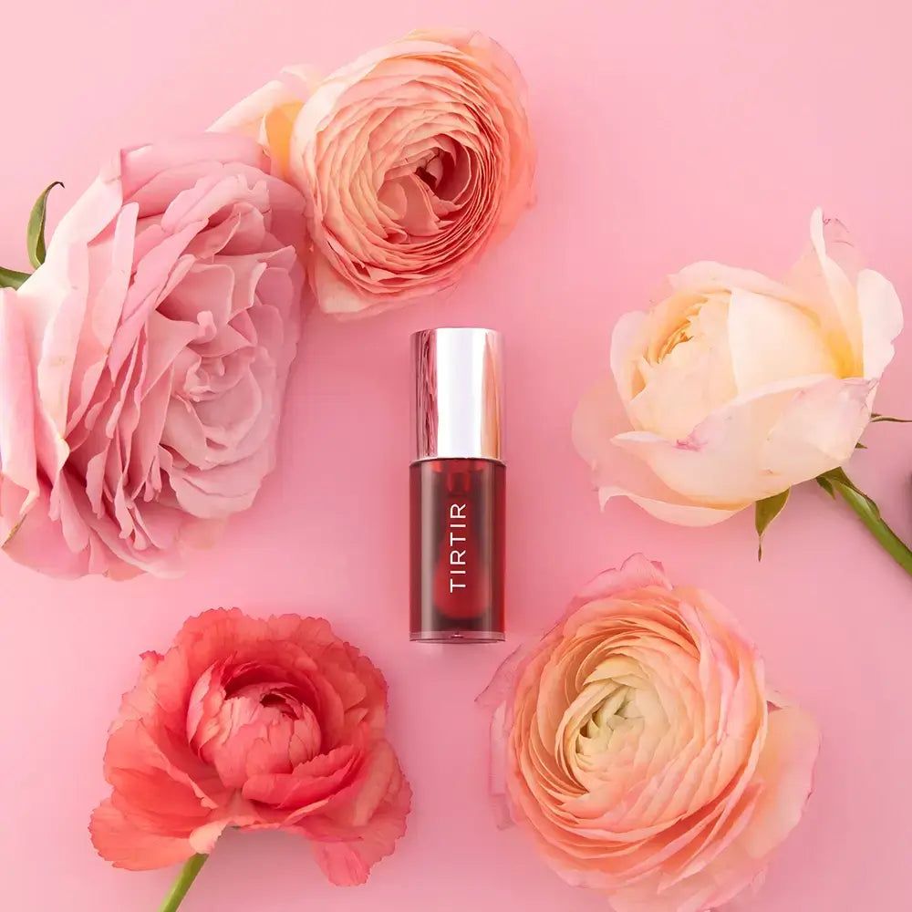 TIR TIR My Glow Lip Oil Rosy sur fond rose, entouré de fleurs roses et oranges.
