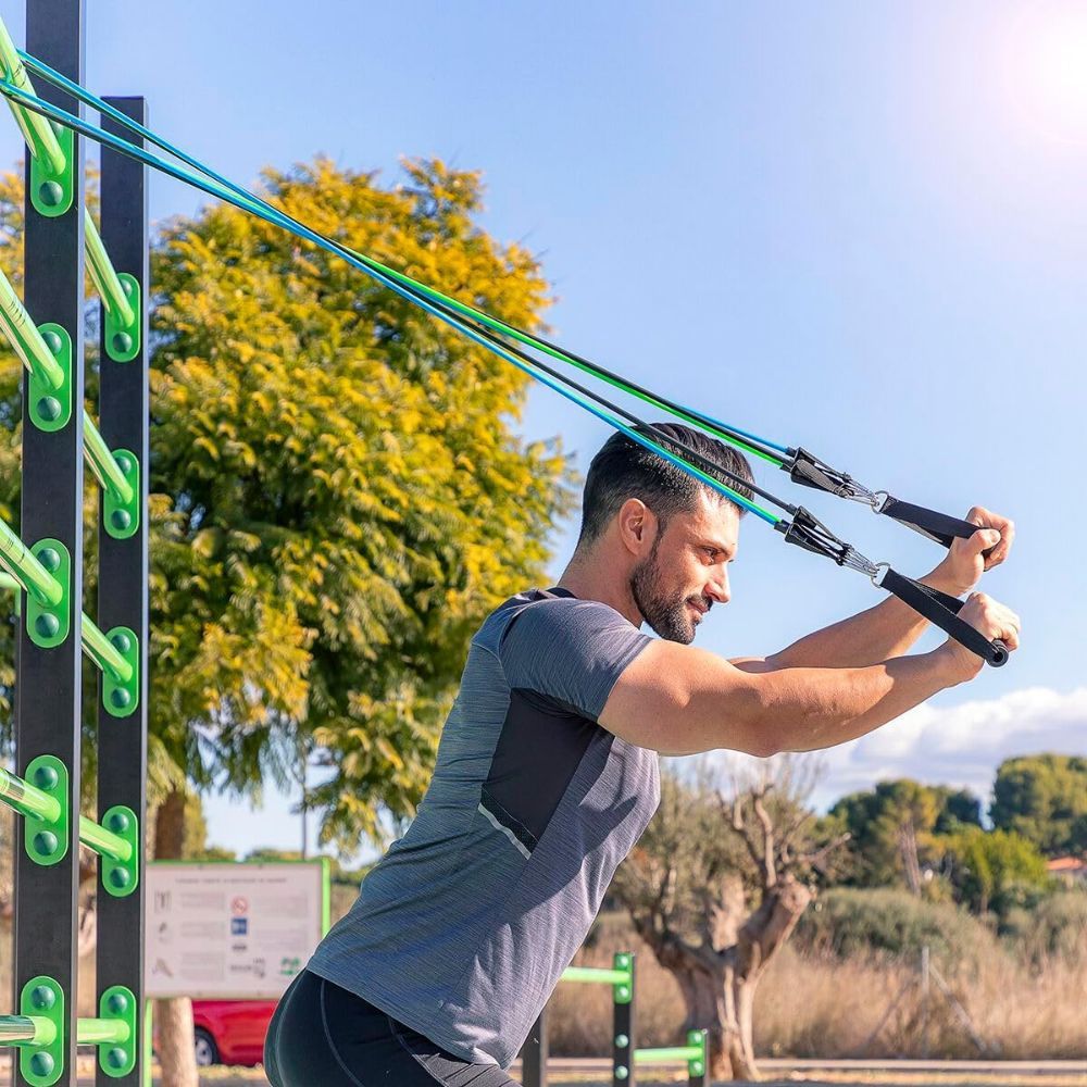 Man die buiten traint met weerstandsbanden. Handvatten en banden in verschillende kleuren. Sportkleding. Groene omgeving.