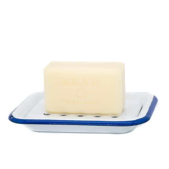 Savon sur porte-savon en émail blanc et bleu. Savon rectangulaire, jaune clair, avec marquage. Porte-savon rectangulaire, perforé, bordé de bleu.