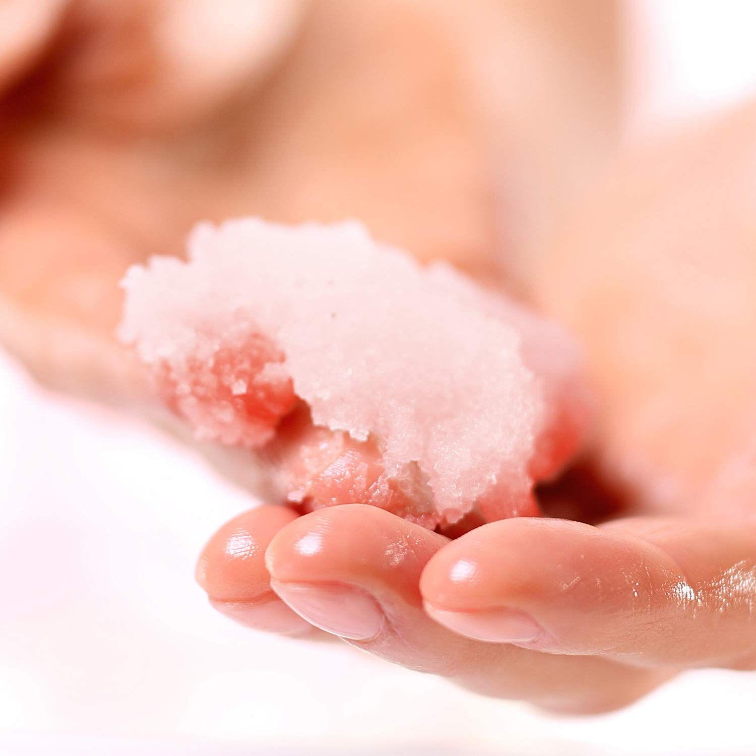 Hand houdt scrub vast. Roze scrub met zout. Lichte huid.