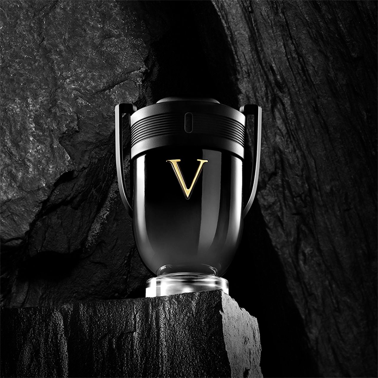 Flacon noir avec marquage "V" doré sur un rocher. Le flacon a un bouchon noir et une base transparente.
