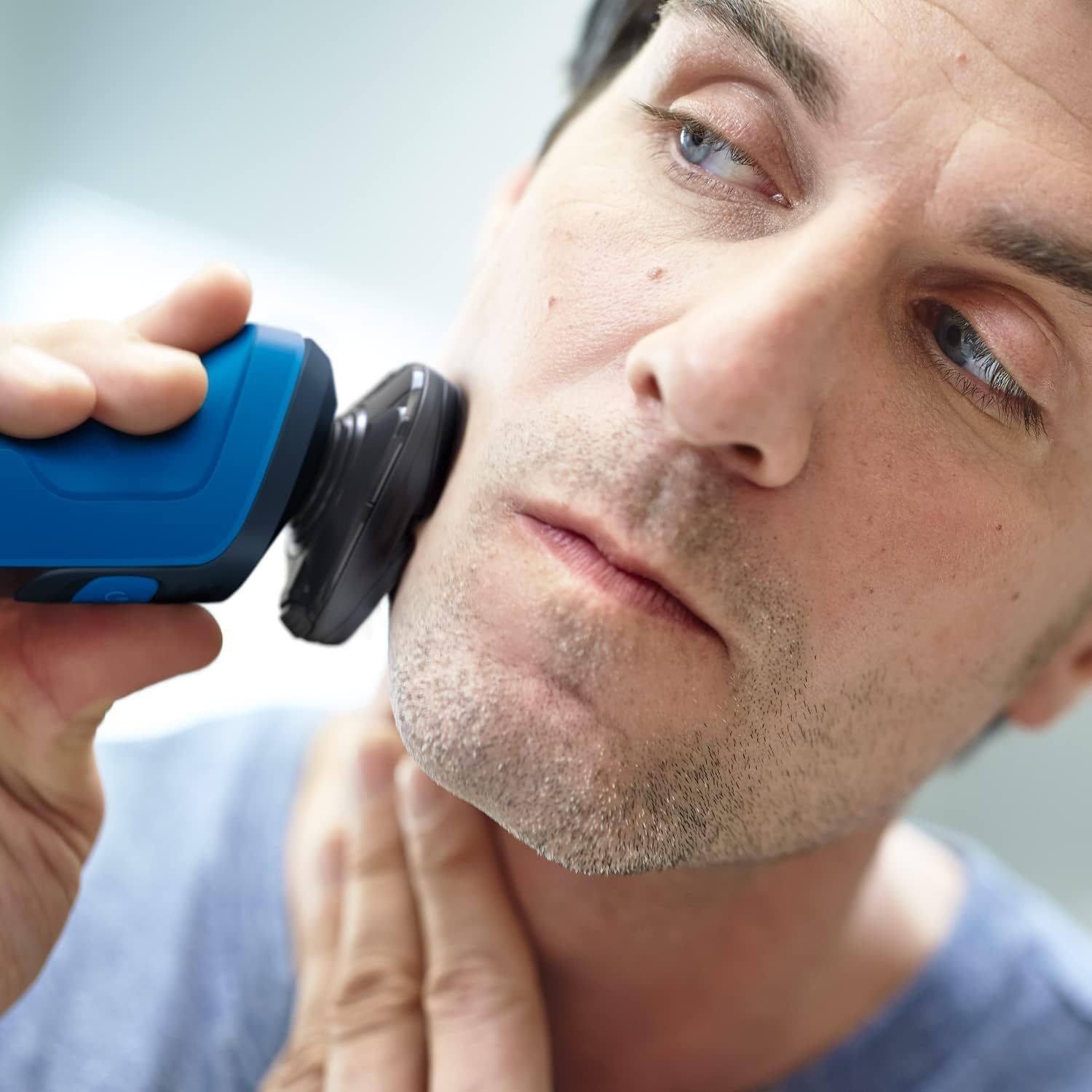 Man scheert zich met blauw elektrisch scheerapparaat. Close-up van gezicht en scheerapparaat.