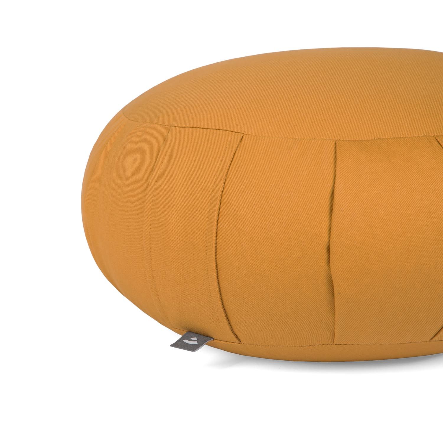 Detailopname van een mosterdkleurig meditatiekussen. Stoffen hoes met verticale naden. Klein label aan de zijkant.