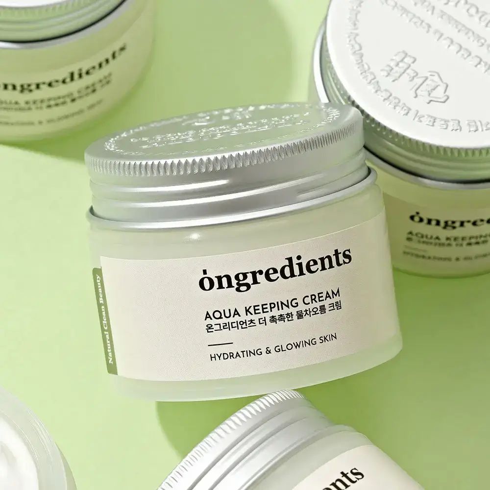 Plusieurs pots de crème avec couvercles argentés. Inscription : Ongredients, Aqua Keeping Cream, Hydrating & Glowing Skin. Sur fond vert.