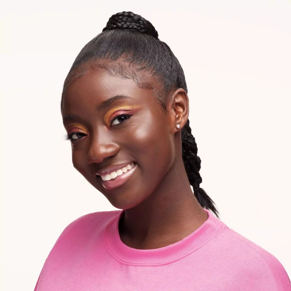 Portret van een jonge vrouw met gevlochten haar. Ze draagt een roze top en make-up.