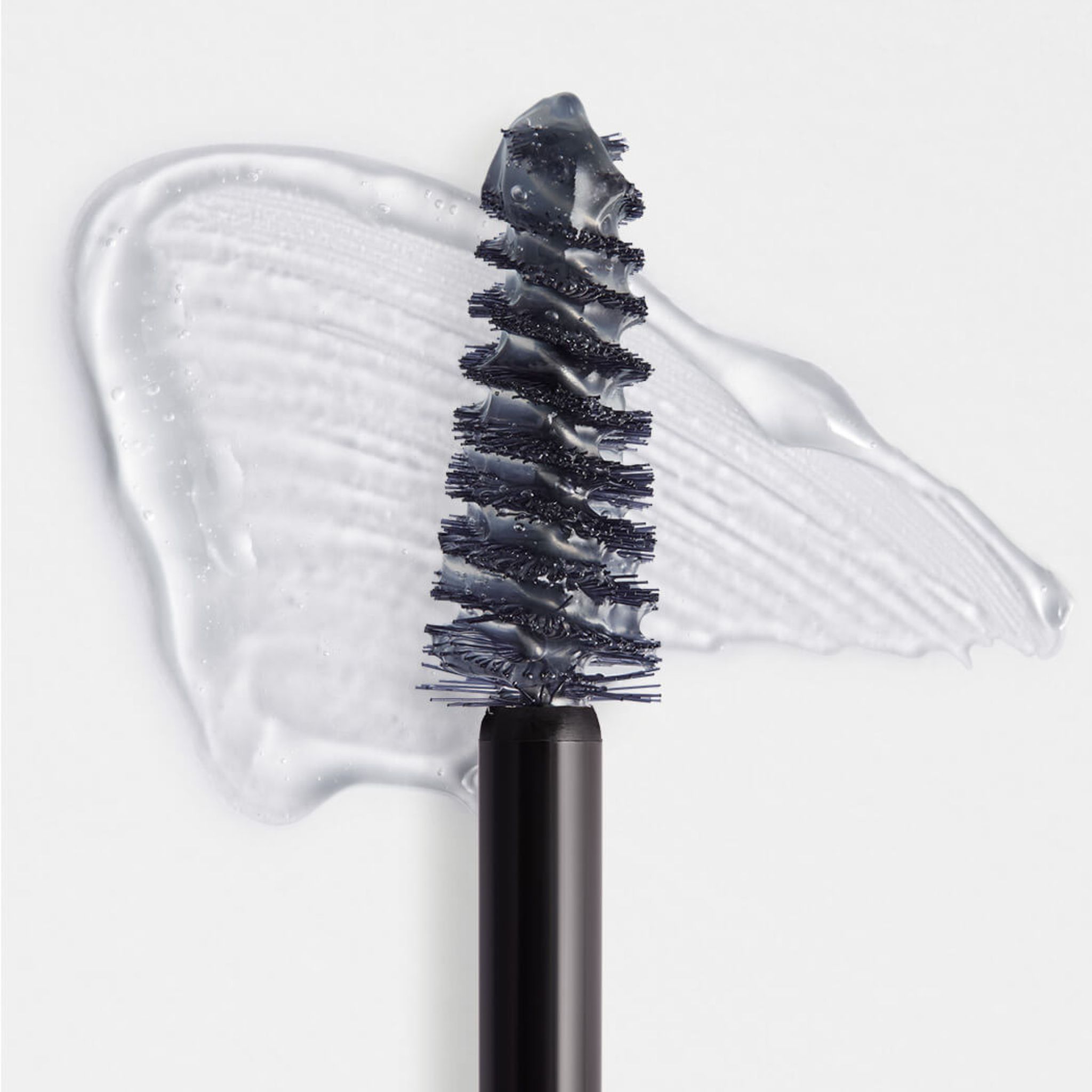 Gros plan d'une brosse à sourcils avec gel transparent et une touche sur fond blanc.