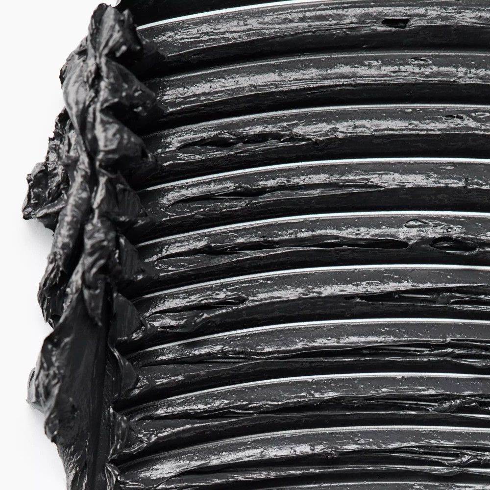 Gros plan sur du mascara noir sur une surface. La texture est épaisse et inégale.