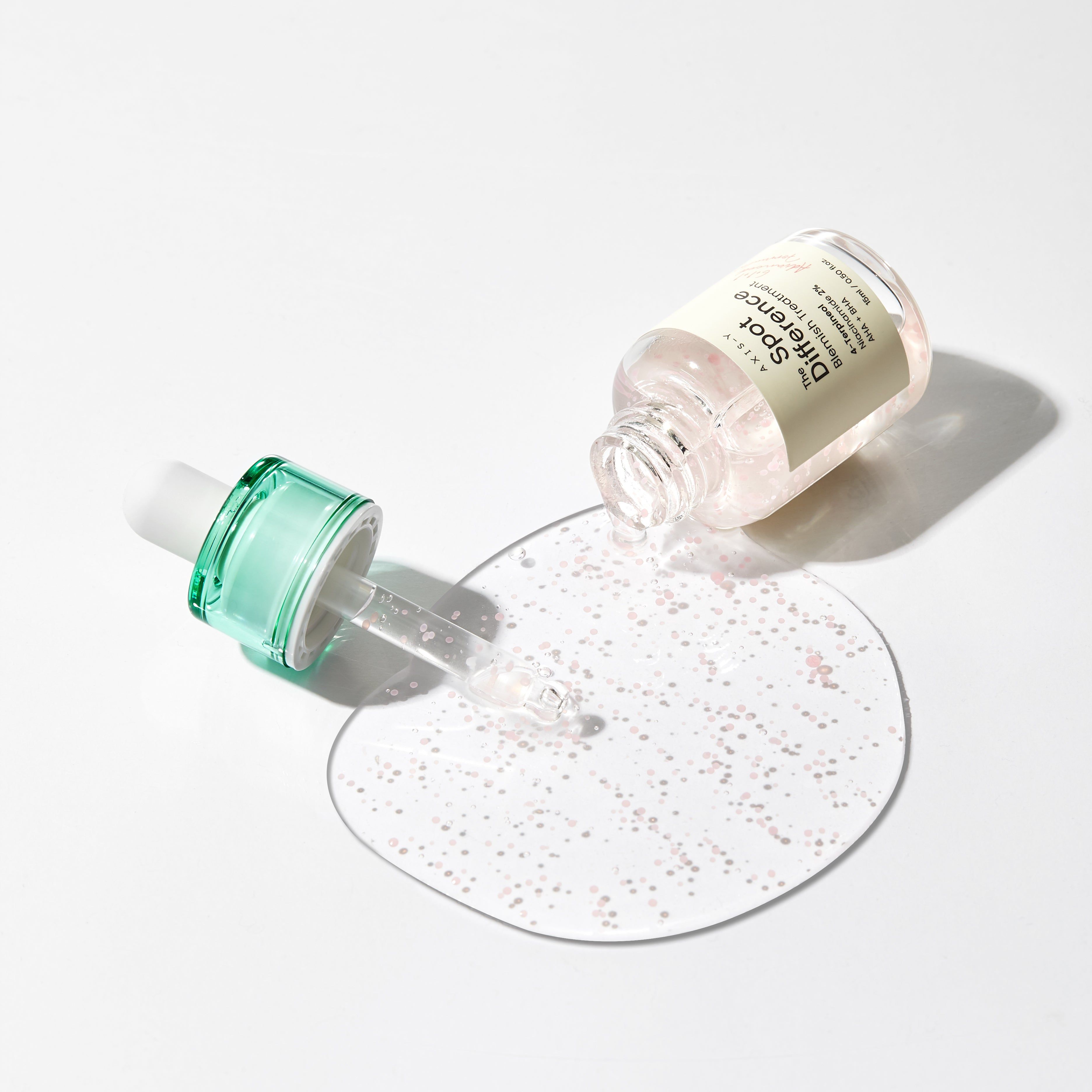 Transparante fles met groene dop en pipet. Vloeistof wordt op een oppervlak gegoten. Productnaam zichtbaar.