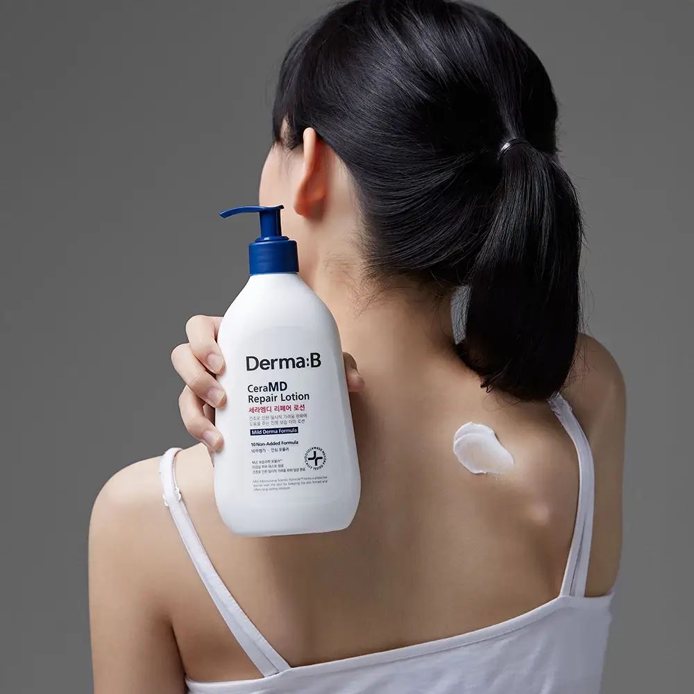 Vrouw houdt witte fles met blauwe pomp vast. Opschrift: Derma:B CeraMD Repair Lotion. Vlek lotion op de rug.
