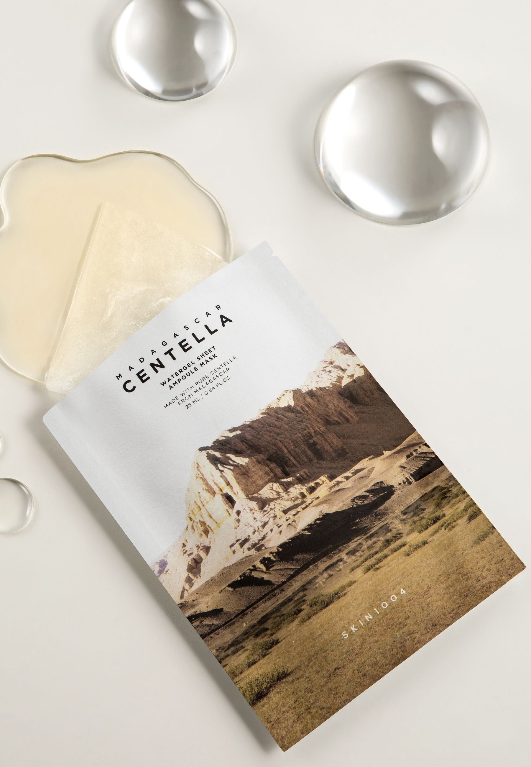Emballage du produit et masque avec image de paysage. Texte: Madagascar Centella Watergel Sheet Ampoule Mask. Accessoires.