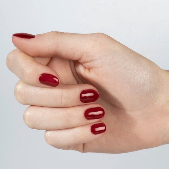 Main avec ongles vernis. Ongles vernis avec du vernis à ongles rouge. Ongles vernis de la couleur Hello Merlot.