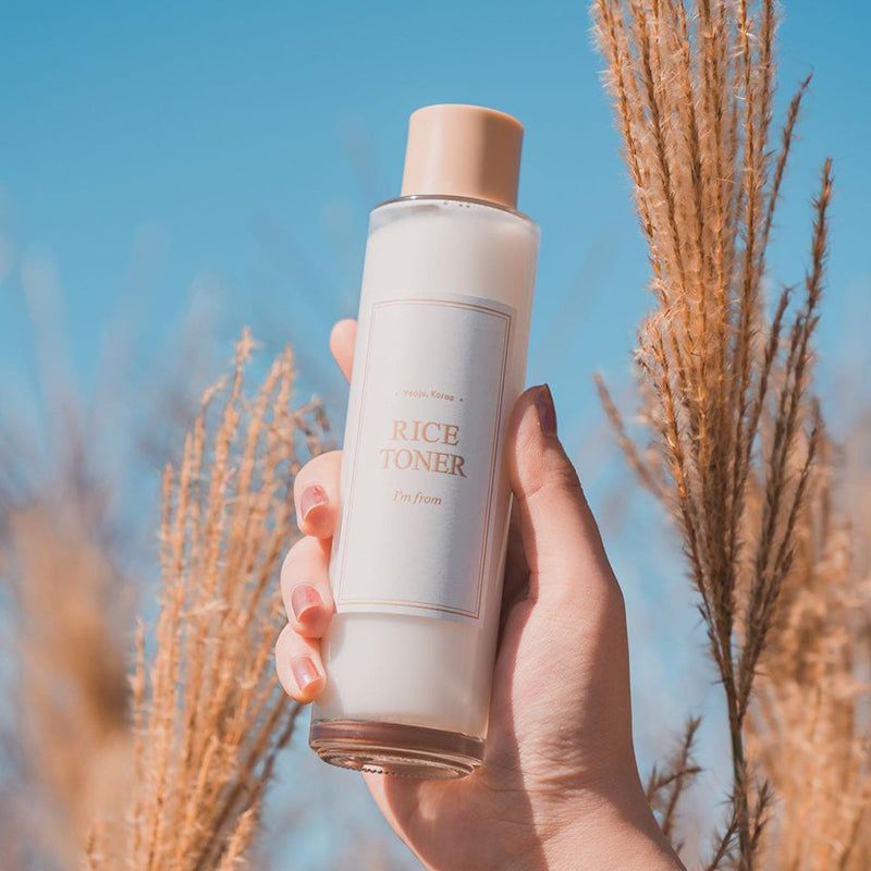 Tonerfles in een hand. Etiket "RICE TONER" en "I'm from". Achtergrond met grassen.