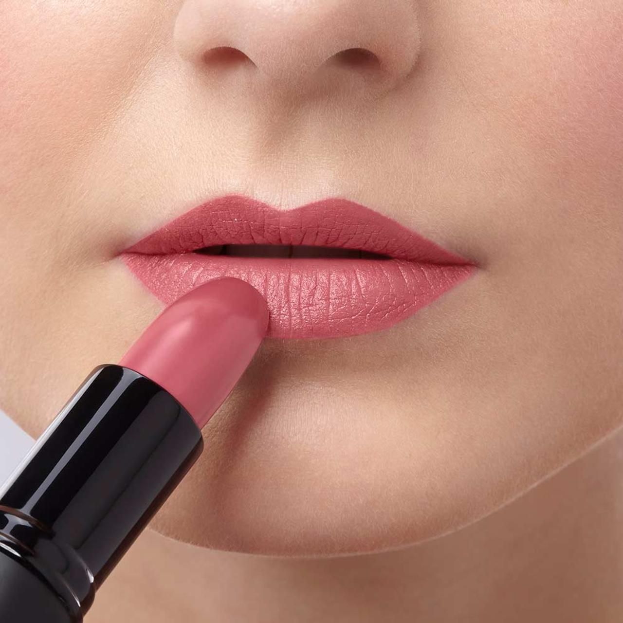 Persoon brengt roze lipstick aan op de lippen. Zwarte lipstick houder zichtbaar.