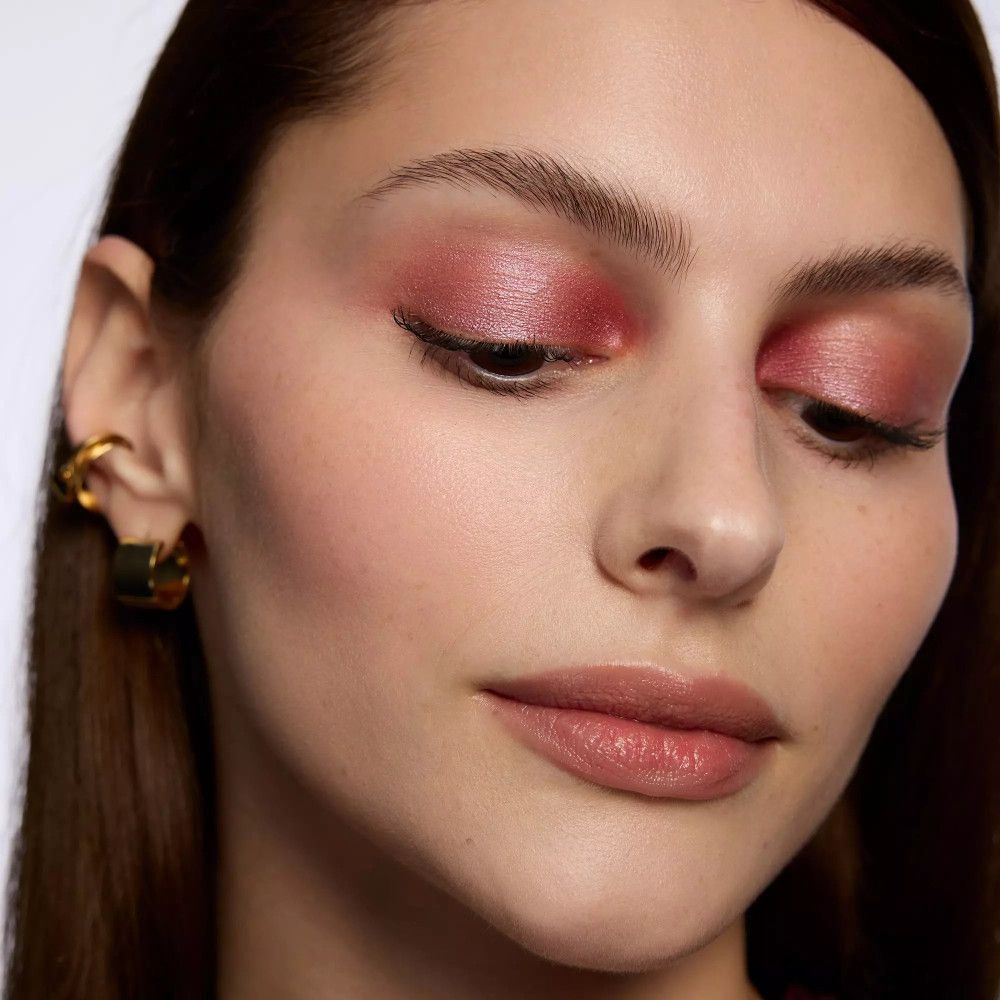 Gros plan d'une femme avec fard à paupières rose. Boucles d'oreilles dorées. Pas de nom de produit ni de marque.