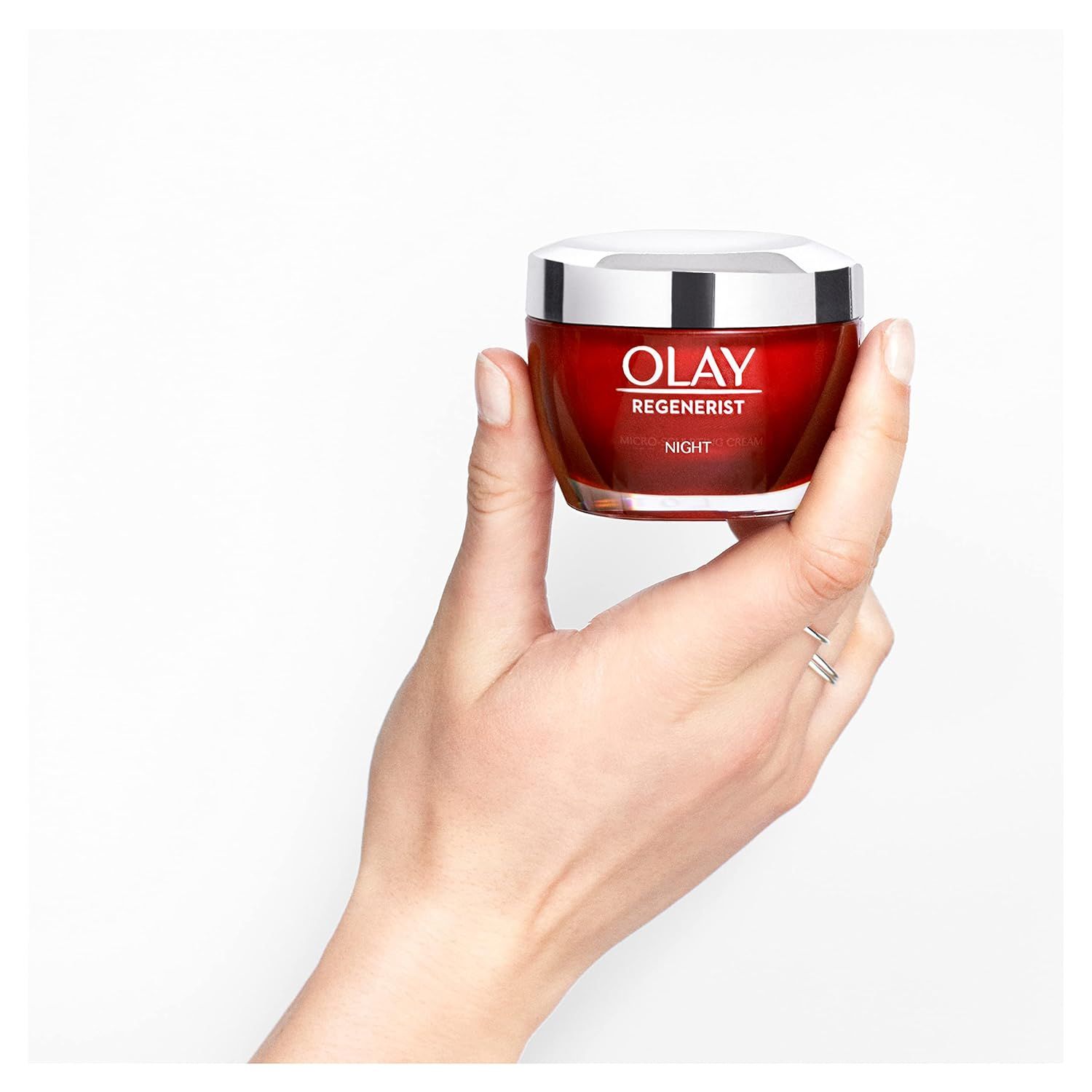 Main tenant un pot de crème rouge avec couvercle argenté. Olay Regenerist Nachtcreme.