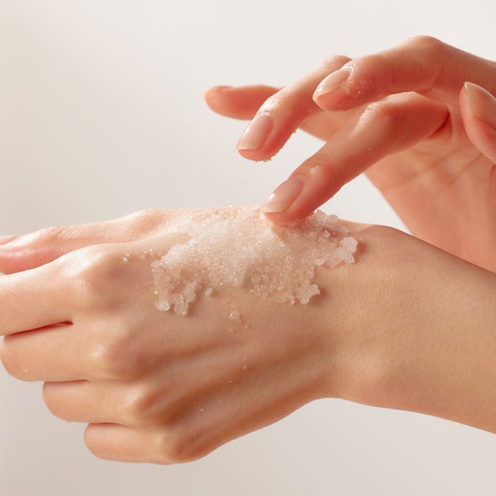 Mains avec produit sur la peau. Le produit est un gommage granuleux.